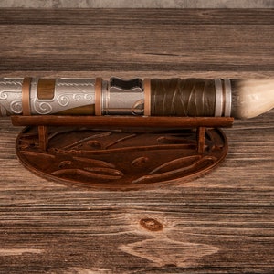 May include: A silver and brown lightsaber with a white tip, resting on a wooden stand with intricate carvings.