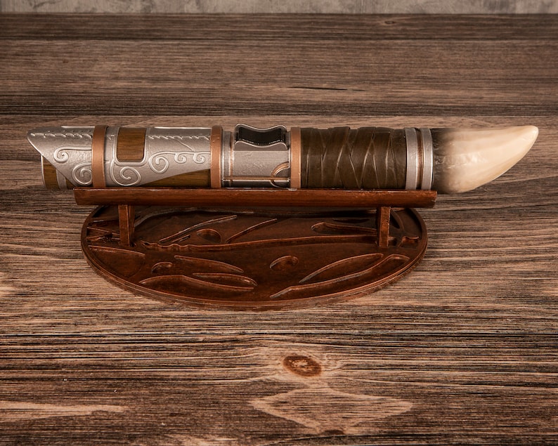 May include: A silver and brown lightsaber with a white tip, resting on a wooden stand with intricate carvings.
