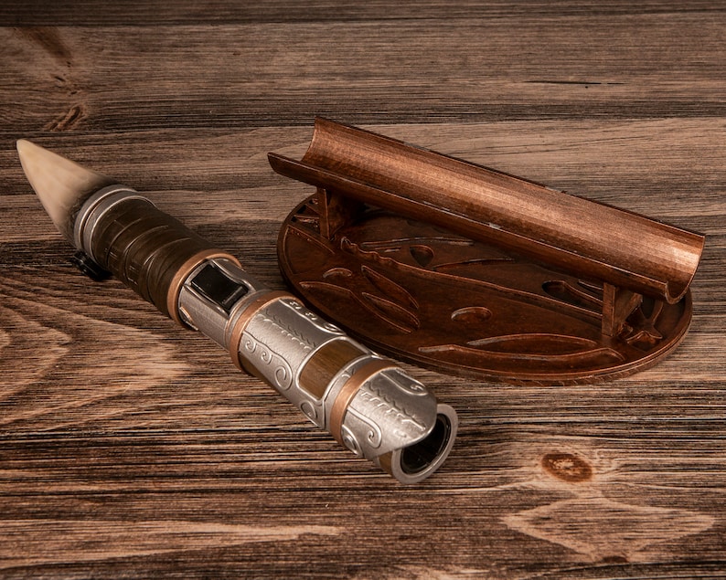 May include: A silver and brown lightsaber with a wooden handle and a decorative stand. The stand is made of wood and has a carved design.