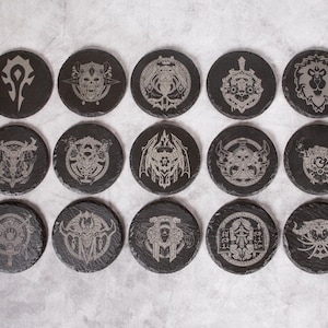 May include: Set of 16 black slate coasters with various silver engraved designs, including a skull, a dragon, a shield, and a wolf. The coasters are circular and have a smooth, polished surface.