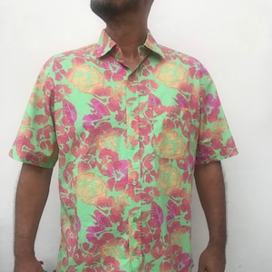 Könnte beinhalten: Ein grünes, kurzärmeliges Hemd mit Knöpfen und einem Blumendruck in Rosa-, Orange- und Gelbtönen.
