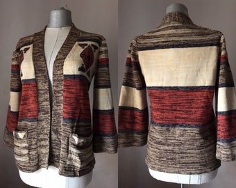 May include: A brown, beige, red, and blue striped cardigan with a geometric pattern on the front. The cardigan has long sleeves and two pockets.