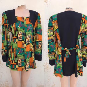 Puede incluir: Una túnica de manga larga con estampado geométrico en tonos naranja, verde, amarillo y negro. La túnica tiene un cuello y puños negros, y un lazo en la espalda.