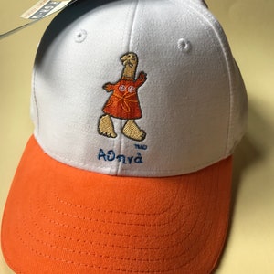 Puede incluir: Gorra de b&eacute;isbol blanca con visera naranja. La gorra presenta un personaje de dibujos animados bordado con un vestido rojo y el texto "the Agnya".