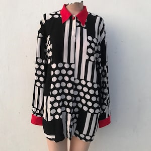 May include: A long-sleeved shirt with a striking black and white pattern of stripes and polka dots. The shirt features a red collar and cuffs, adding a bold contrast to the monochrome design. The shirt is displayed on a mannequin.