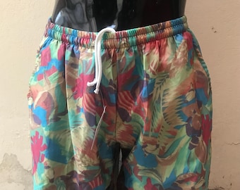 May include: Multicolored swim trunks with a tropical print featuring leaves and flowers. The trunks have a drawstring waist.
