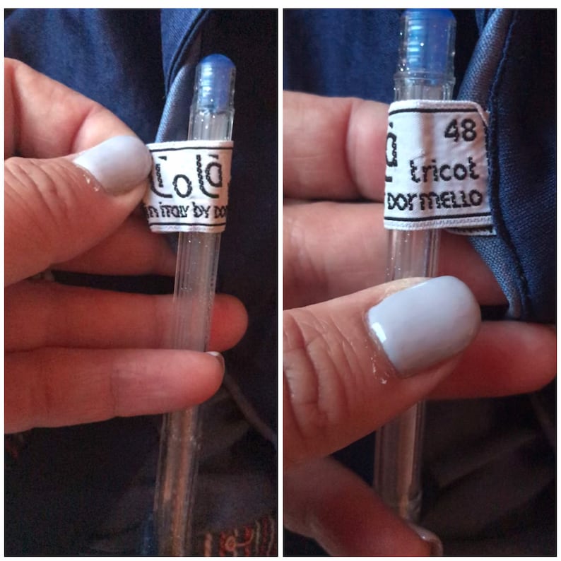 May include: A white label with black text that reads "Lola in Italy by Dora" attached to a clear pen. The label is attached to the pen with a blue cap.