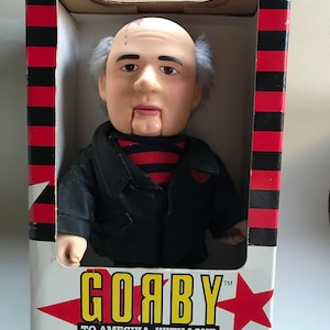May include: A vintage ventriloquist dummy doll in its original box. The doll has a bald head with gray hair, a black jacket, and a red and black striped shirt. The box reads "GOABY" and "TO AMEЯIKA, WITH LOVE."