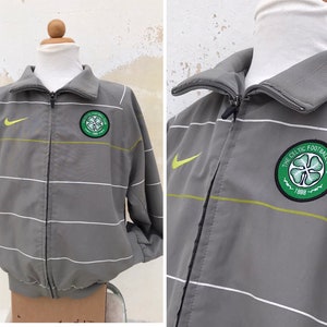 May include: Grey and white striped zip-up jacket with a green Celtic Football Club logo on the right side and a Nike swoosh on the left side.