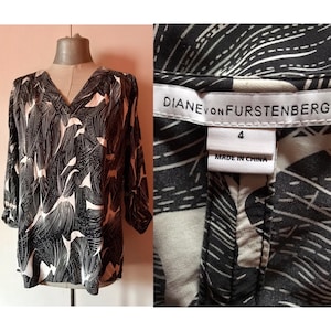 Könnte beinhalten: Schwarz-weiß gemusterte Bluse mit V-Ausschnitt und 3/4-Ärmeln. Die Bluse trägt den Schriftzug "Diane von Furstenberg" und "Made in China" auf dem Etikett.