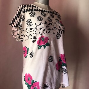 May include: White short-sleeved shirt with a black and white checkered pattern, black and white circles, and pink flowers.