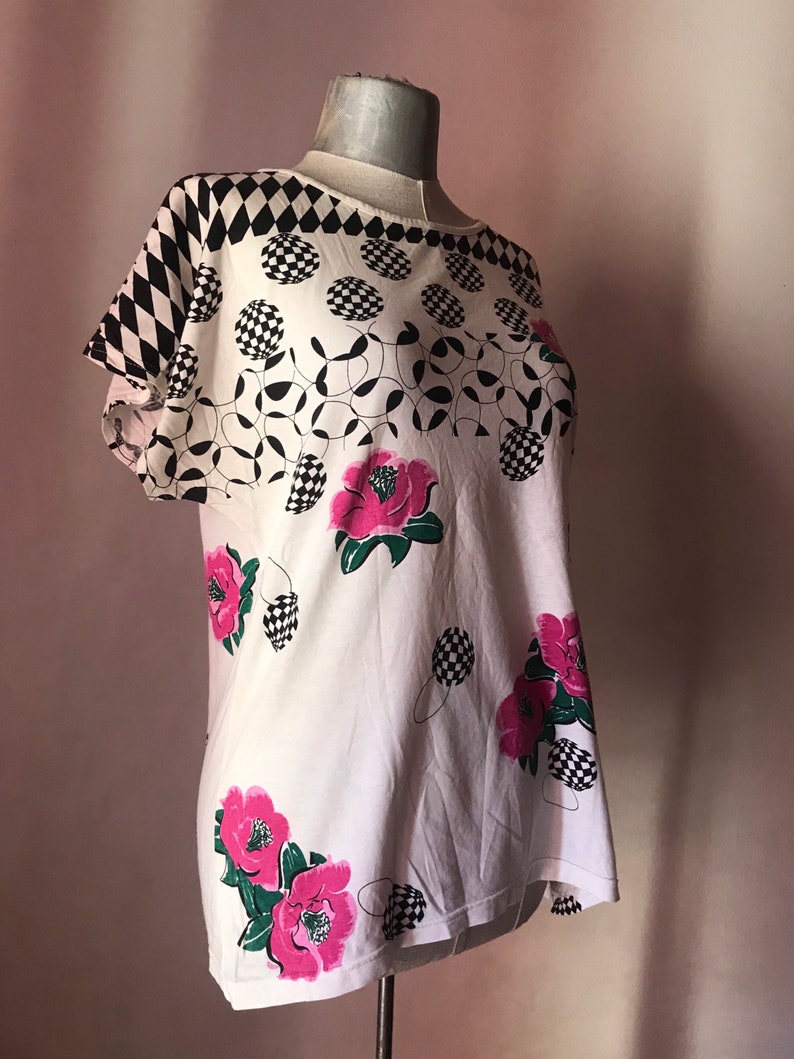 May include: White short-sleeved shirt with a black and white checkered pattern, black and white circles, and pink flowers.