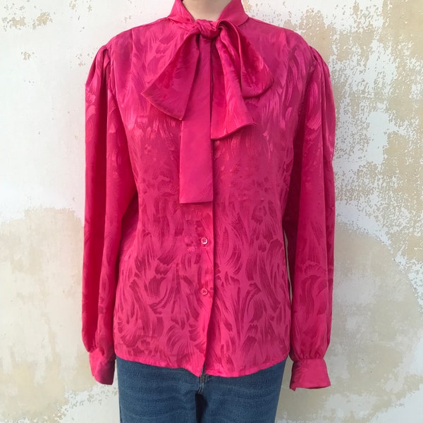 Satiny, embossed, bow collared 80s vintage shirt features shoulder pads in bright fuchsia pink color
