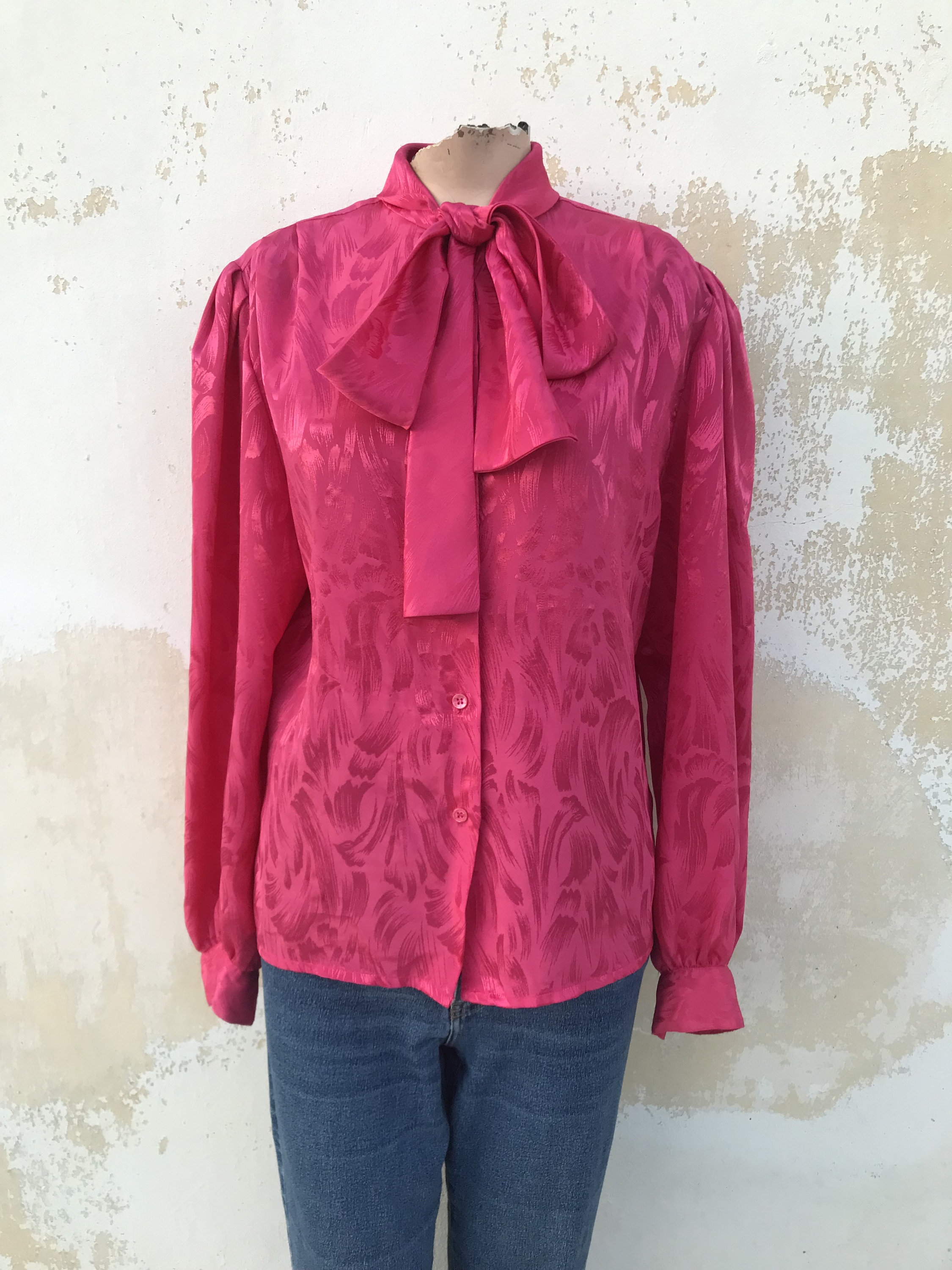Satiny, embossed, bow collared 80s vintage shirt features shoulder pads in bright fuchsia pink color