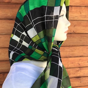 Puede incluir: Una bufanda a cuadros verdes, negros y blancos con un patrón geométrico. La bufanda está atada alrededor del cuello de un maniquí.