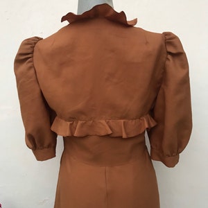 May include: A brown dress with a ruffled collar and sleeves. The dress has a fitted bodice and a flowing skirt.