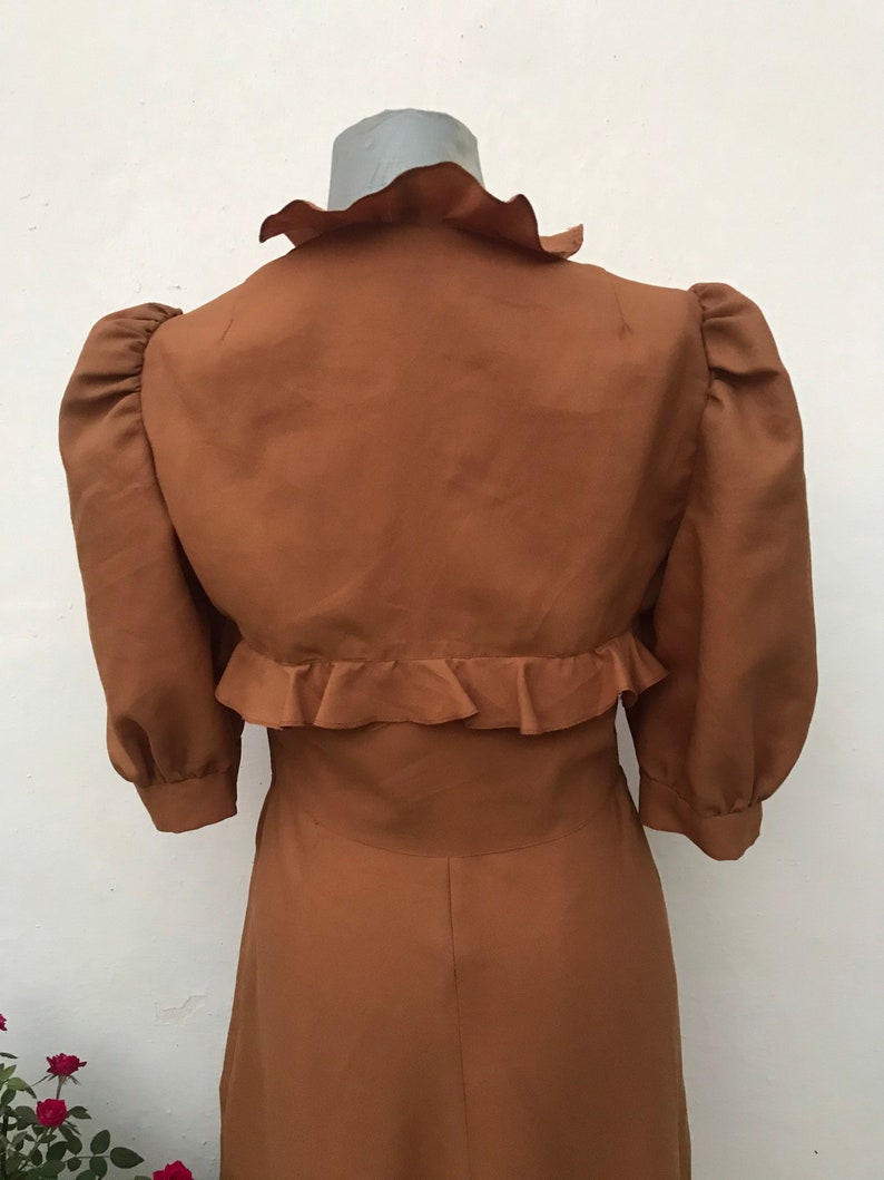 May include: A brown dress with a ruffled collar and sleeves. The dress has a fitted bodice and a flowing skirt.