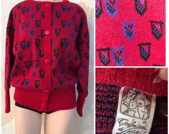 Berry red cardigan 1980s vintage, features emblems in blue. Retro knitwear sweater with golden yarns and wide ribbed waistband