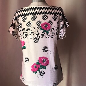 May include: White short-sleeved shirt with a black and white checkered pattern, pink flowers, and black and white circles.