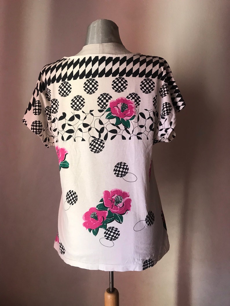 May include: White short-sleeved shirt with a black and white checkered pattern, pink flowers, and black and white circles.