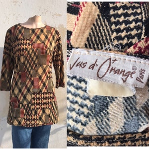May include: A brown, black, and red plaid long-sleeved shirt with a round neckline. The shirt has a patchwork design and is made of a soft, stretchy fabric. The shirt has a label that reads "Jus d'Orange Paris".