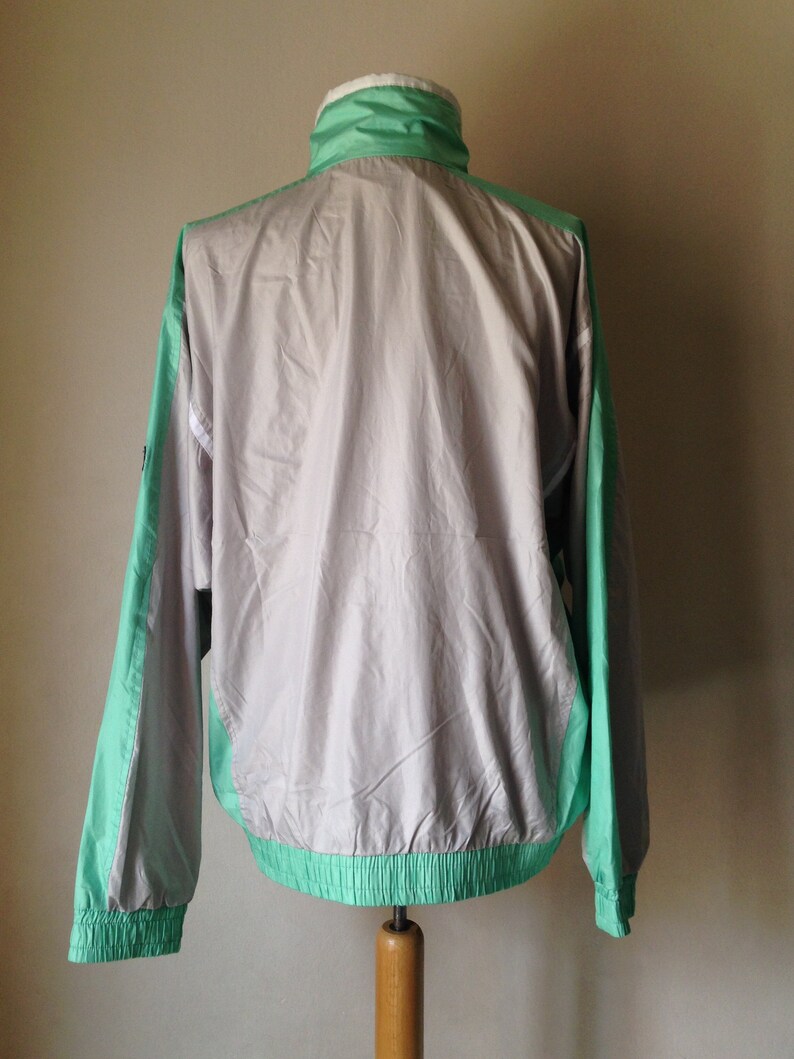 Puede incluir: Chaqueta cortavientos vintage en color gris claro con detalles en verde menta y blanco. La chaqueta tiene cuello alto, pu&ntilde;os el&aacute;sticos y dobladillo con cord&oacute;n. Las mangas y los laterales son verde menta.