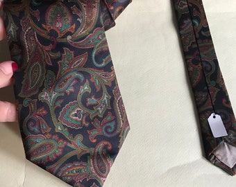 Könnte beinhalten: Eine dunkelbraune Krawatte mit Paisley-Muster in einem grün-braun-burgunderfarbenen Farbschema. Die Krawatte ist gefaltet und auf einer hellbeigen Oberfläche ausgelegt.