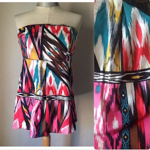 Könnte beinhalten: Ein trägerloses Oberteil mit einem bunten geometrischen Muster in den Farben Pink, Blau, Braun und Weiß. Das Oberteil hat einen figurbetonten Oberkörper und einen fließenden Rock.