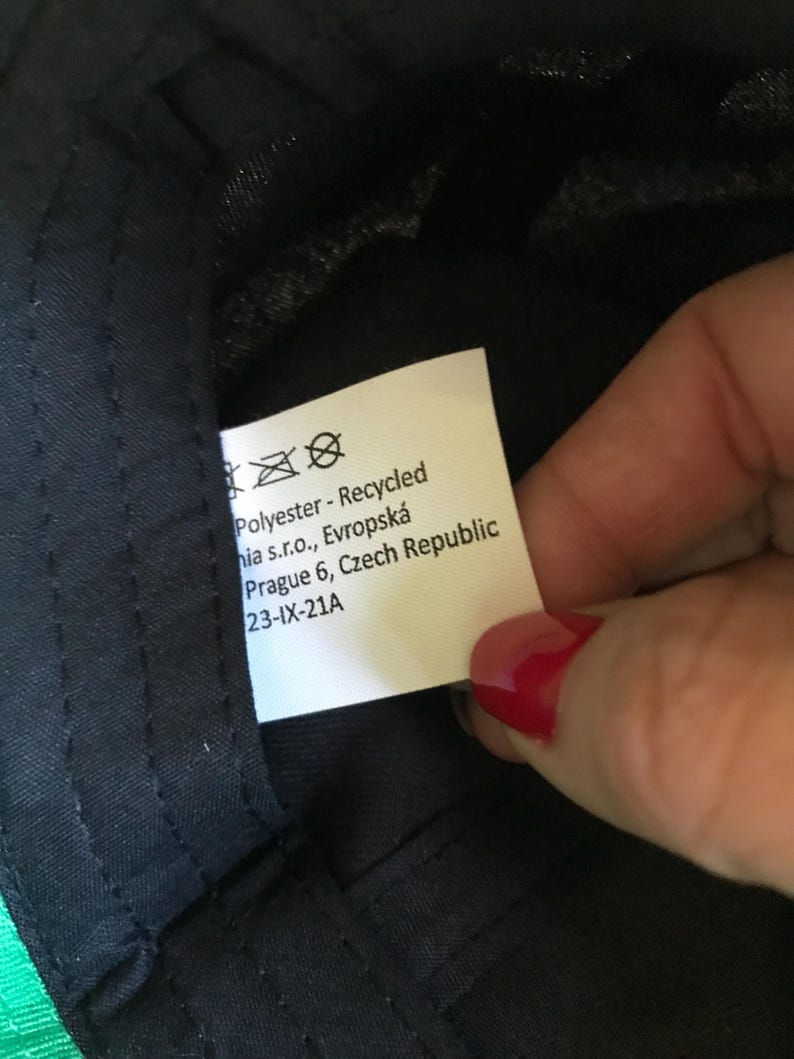 Op de afbeelding: Wit etiket met zwarte tekst die "Polyester - Gerecycled hia s.r.o., Evropsk&aacute; Praag 6, Tsjechische Republiek 23-IX-21A" luidt.