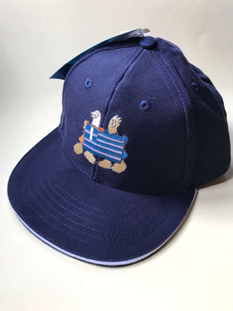 Puede incluir: Una gorra de b&eacute;isbol azul marino con visera blanca. La gorra presenta un dise&ntilde;o bordado de dos ping&uuml;inos sosteniendo una bandera griega.