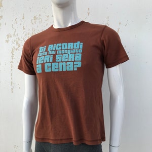 May include: A brown t-shirt with a blue graphic that says "Ti Ricordi cosa hai mangiato ieri sera a cena?"