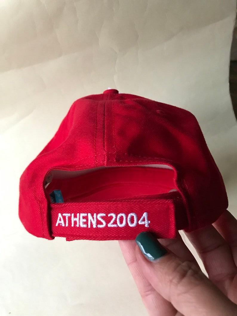 Puede incluir: Gorra de b&eacute;isbol roja con bordado blanco que dice "ATHENS 2004".
