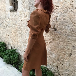 May include: A brown dress with a ruffled collar and puffed sleeves. The dress is knee-length and has a fitted bodice.