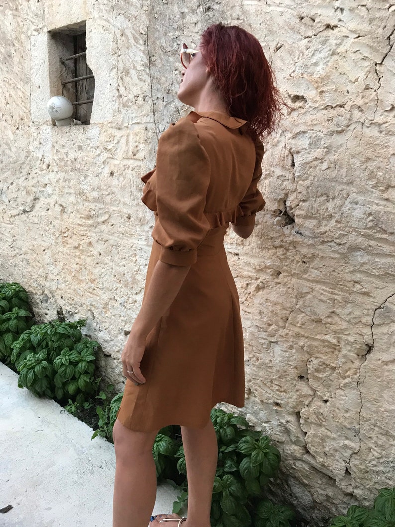 May include: A brown dress with a ruffled collar and puffed sleeves. The dress is knee-length and has a fitted bodice.