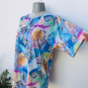 May include: A colorful, abstract print short-sleeved shirt with a blue, yellow, green, and purple design. The shirt is on a white mannequin.