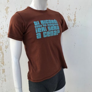 May include: A brown t-shirt with a blue graphic that says "Ti Ricordi cosa hai mangiato ieri sera a cena?"