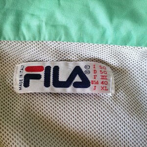 Puede incluir: Primer plano de una etiqueta Fila, con el nombre de la marca en azul marino, rojo y blanco. La etiqueta est&aacute; cosida sobre una tela de malla beige claro, con una tela verde menta encima. La etiqueta indica que la prenda fue fabricada en Italia.