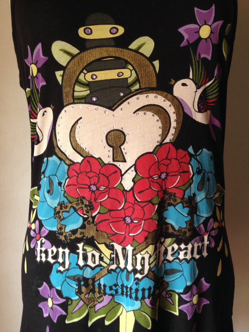 Op de afbeelding: Zwart tanktop met een kleurrijke grafische print van een hart met een sleutelgat, bloemen en vogels. De tekst "Key to My Heart" is gedrukt op de voorkant van het shirt.
