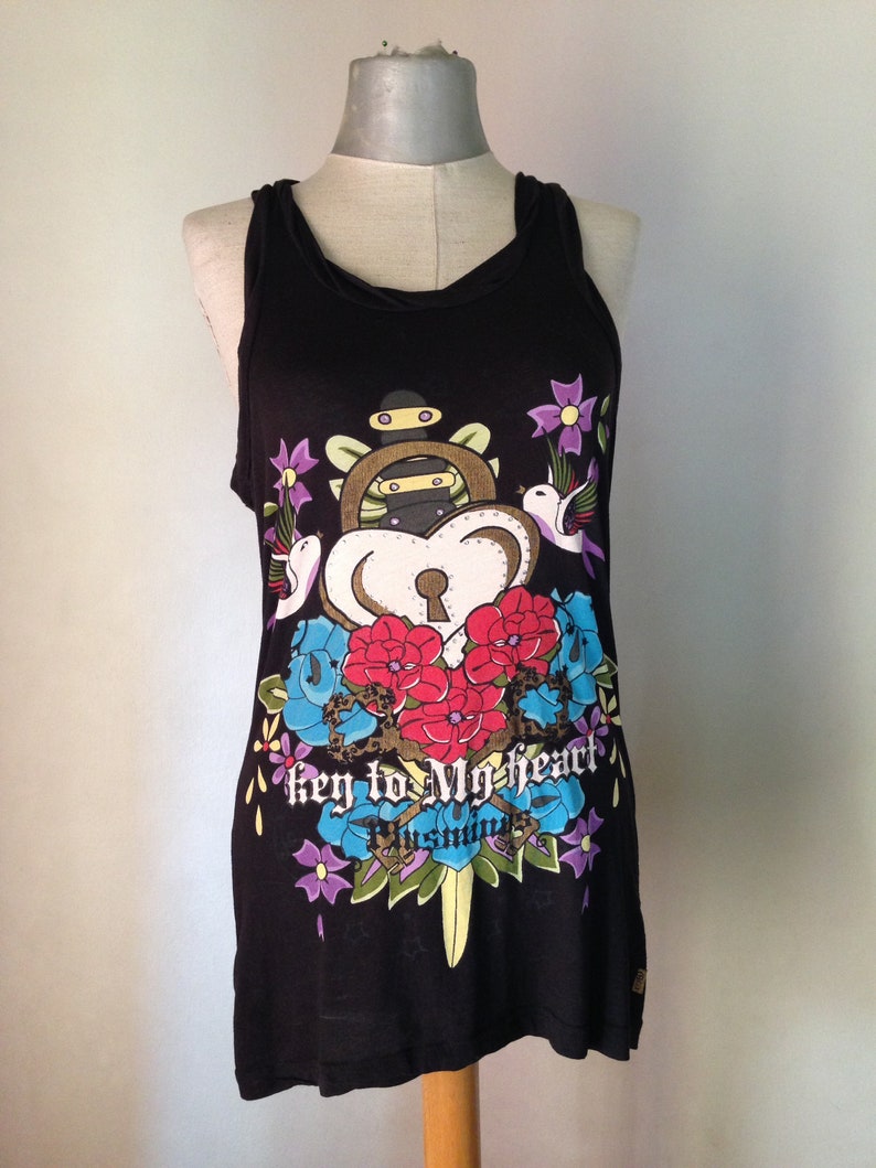 Op de afbeelding: Zwart tanktop met een kleurrijke grafische print van een sleutelgat, bloemen en vogels. De tekst "key to my heart" is onder de print gedrukt.