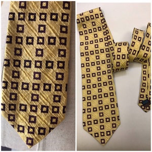Op de afbeelding: Een gele zijden stropdas met een herhalend patroon van donkerbruine vierkanten. De stropdas heeft een puntige punt en is gemaakt van een textuurstof.