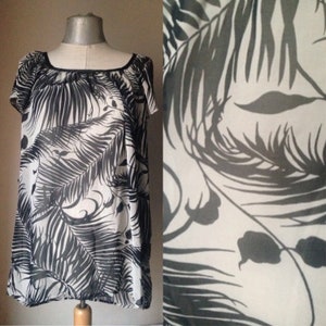 May include: A white sheer blouse with a black and white tropical leaf print. The blouse has a scoop neck and short sleeves.