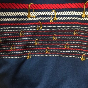May include: A navy blue fabric with a repeating pattern of red and white rope with gold hooks.