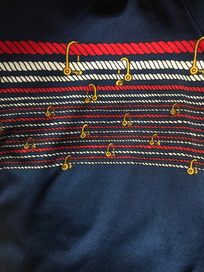 May include: A navy blue fabric with a repeating pattern of red and white rope with gold hooks.