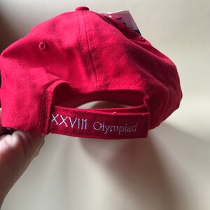 Puede incluir: Gorra de b&eacute;isbol roja con bordado blanco que dice "XXVIII Olympiad".