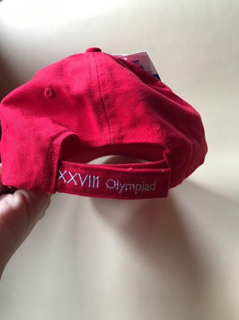 Puede incluir: Gorra de b&eacute;isbol roja con bordado blanco que dice "XXVIII Olympiad".