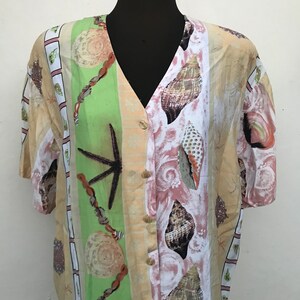 May include: A beige, green, pink and white button-up shirt with a seashell print. The shirt has a V-neck and short sleeves.
