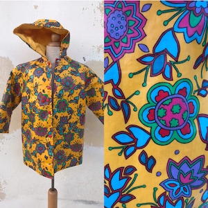 Op de afbeelding: Een gele regenjas met een kleurrijk bloemenpatroon. De regenjas heeft een capuchon en een knoopsluiting.