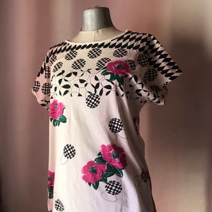 May include: White short-sleeved shirt with a black and white checkered pattern, black and white circles, and pink flowers.