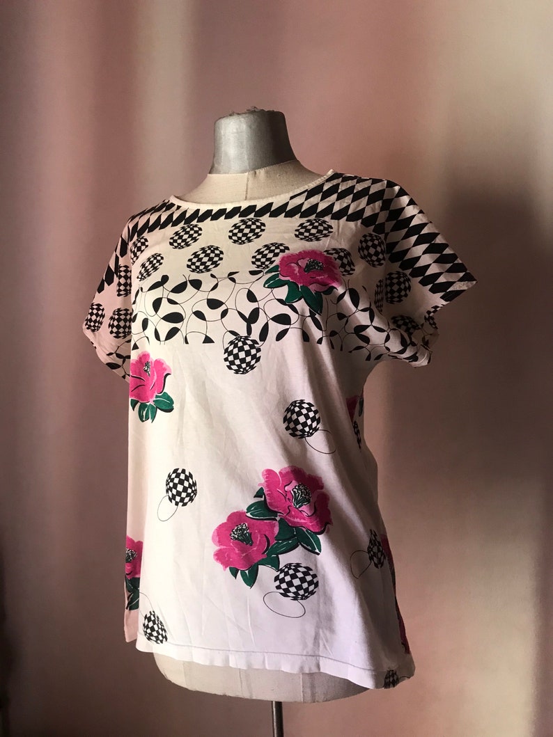 May include: White short-sleeved shirt with a black and white checkered pattern, black and white circles, and pink flowers.