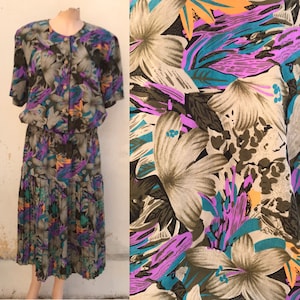 Könnte beinhalten: Ein Vintage-Kleid mit floralem Druck, einem Knopfbodice und einem gerafften Rock. Das Kleid ist aus einem leichten Stoff gefertigt und hat ein farbenfrohes Muster aus Blumen und Blättern in den Farben Lila, Türkis, Orange und Braun.